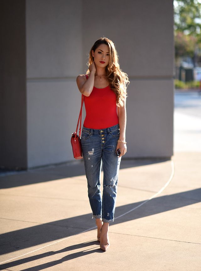 Woman wearing a red ribbed tank top, distressed blue jeans, and nude pointed-toe heels, carrying a red crossbody bag