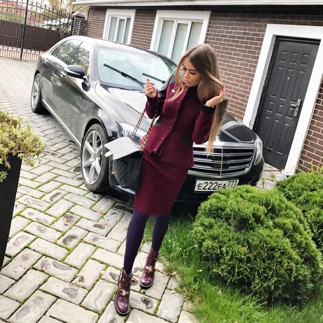 Woman in a burgundy fitted blazer and matching skirt, paired with purple tights and burgundy ankle boots
