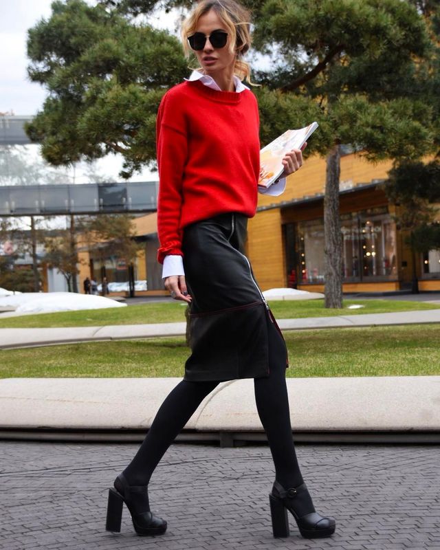 Woman wearing a red sweater, white collared shirt, black leather pencil skirt, black tights, and black platform heels