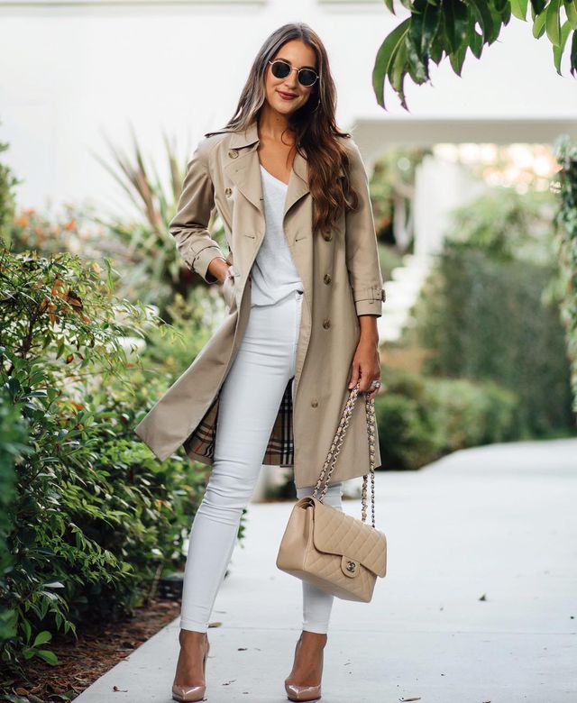 Woman wearing a beige trench coat, white t-shirt, white skinny jeans, and nude high heels, carrying a quilted handbag